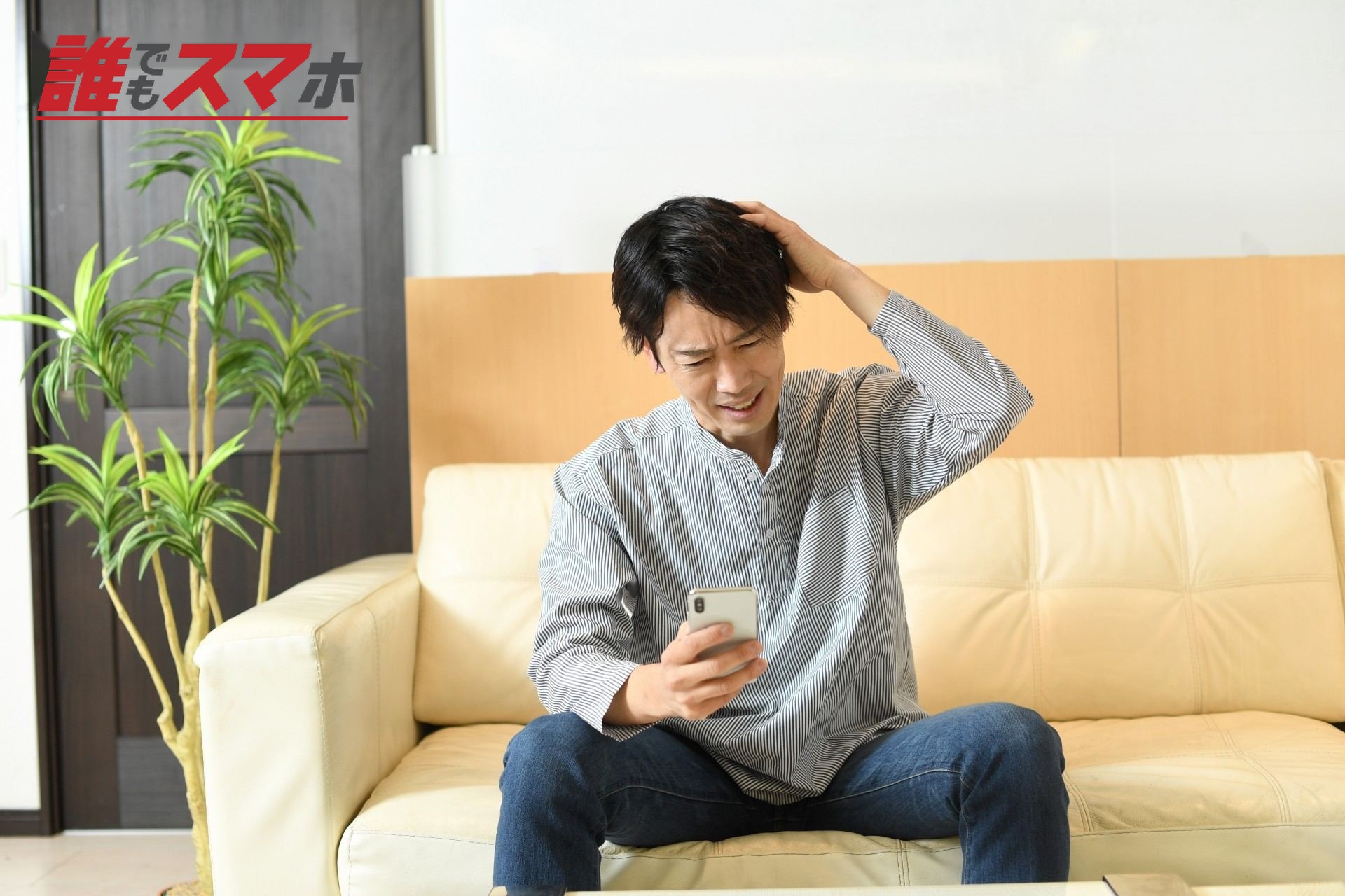 頭を抱えながらスマホを見るアジア人男性