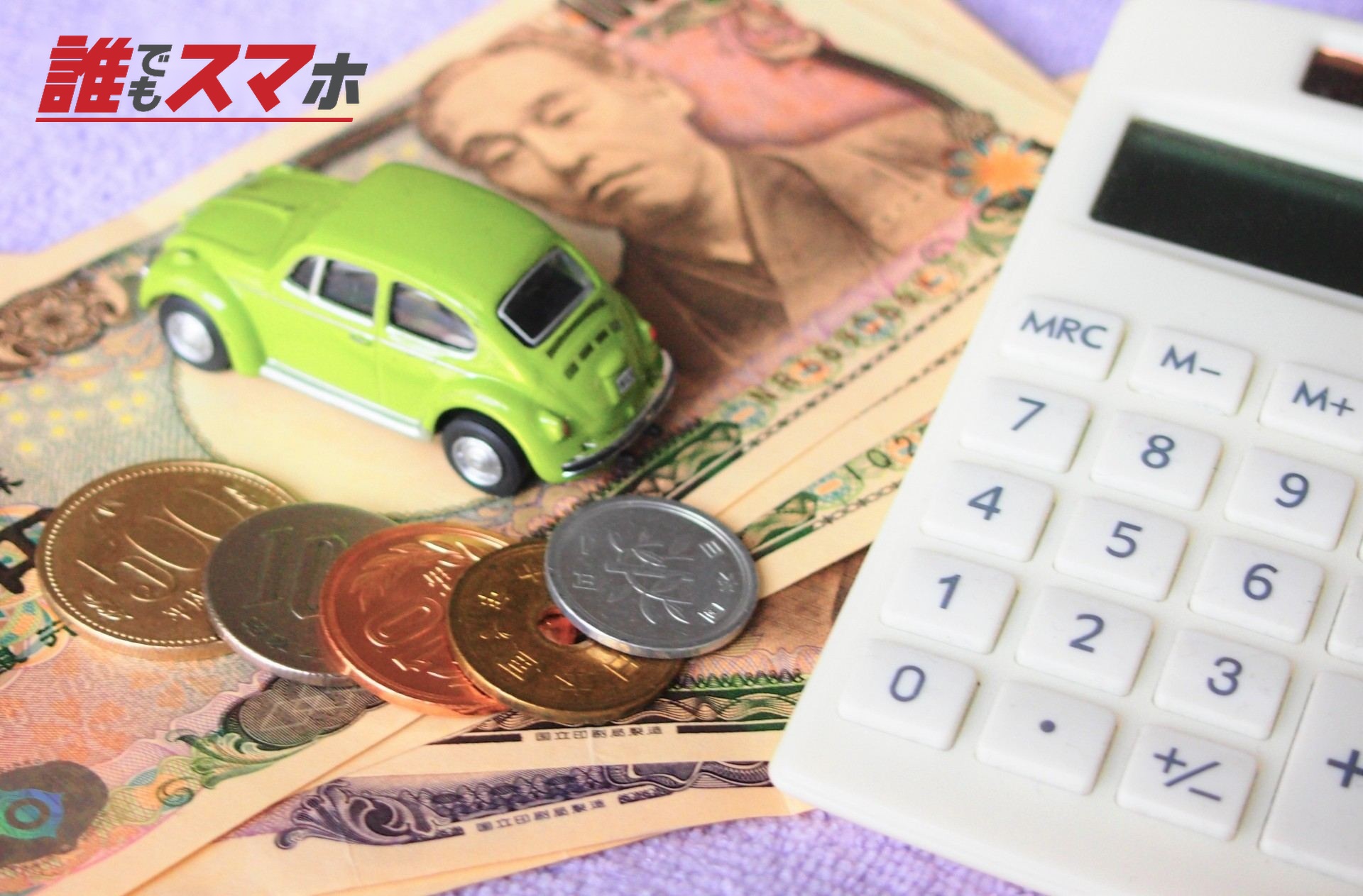 現金の上に乗る車のおもちゃと電卓