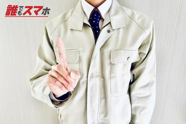 人差し指を立てる作業着姿の男性