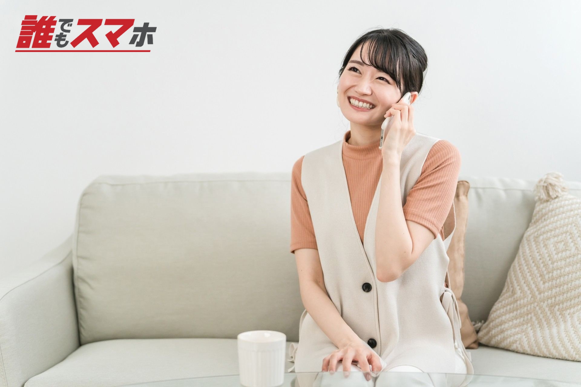 ソファに座ってスマホで電話する笑顔の女性