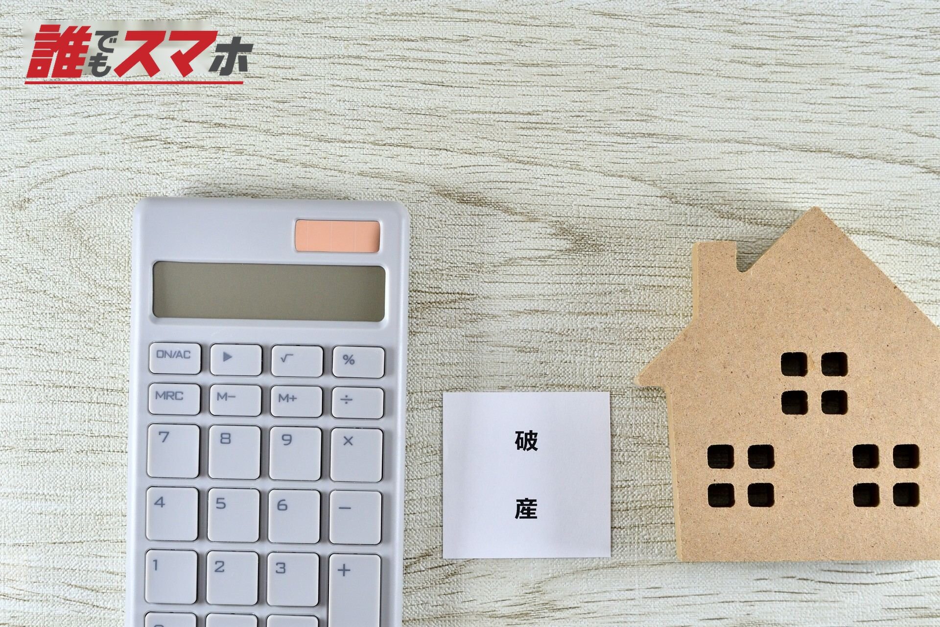 電卓と破産と書いたメモと木て作った家のオブジェ