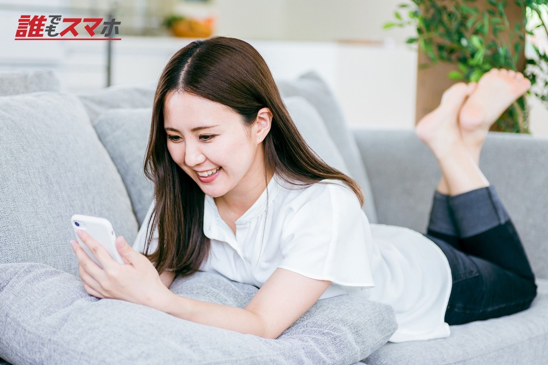 ソファで寝転んでスマホを使う女性