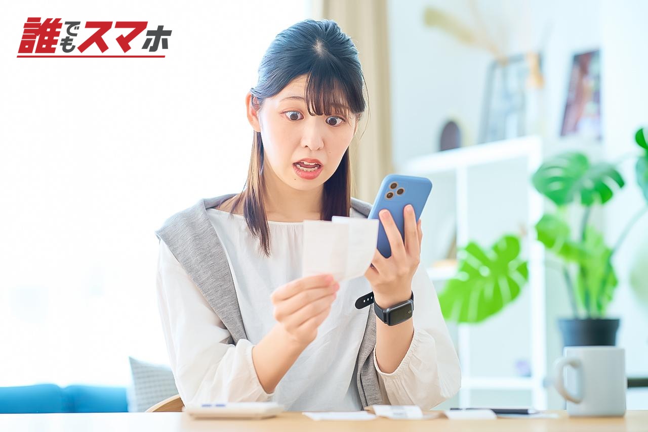 スマートフォンと紙を見て驚く女性