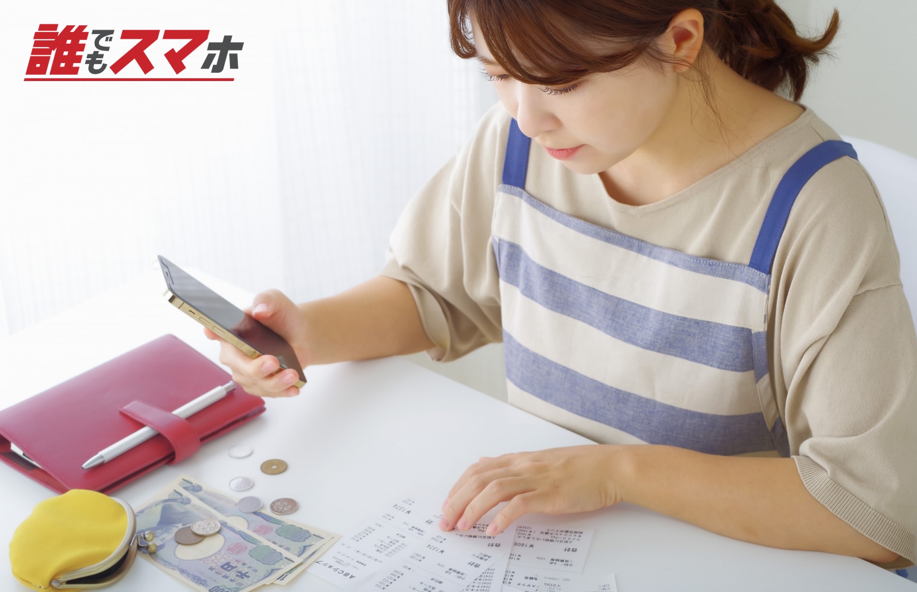 スマートフォンを見ながら家計簿を書く女性