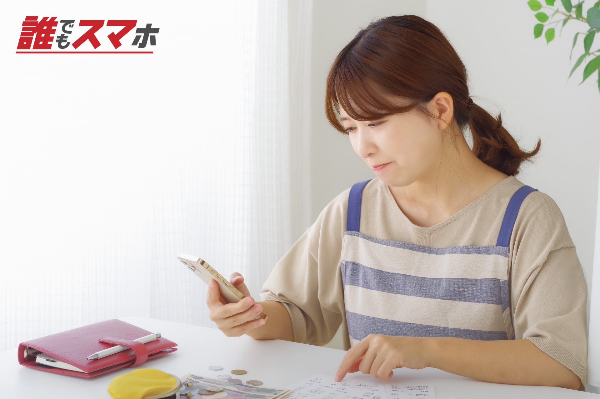 家計簿を前にスマートフォンを見る女性