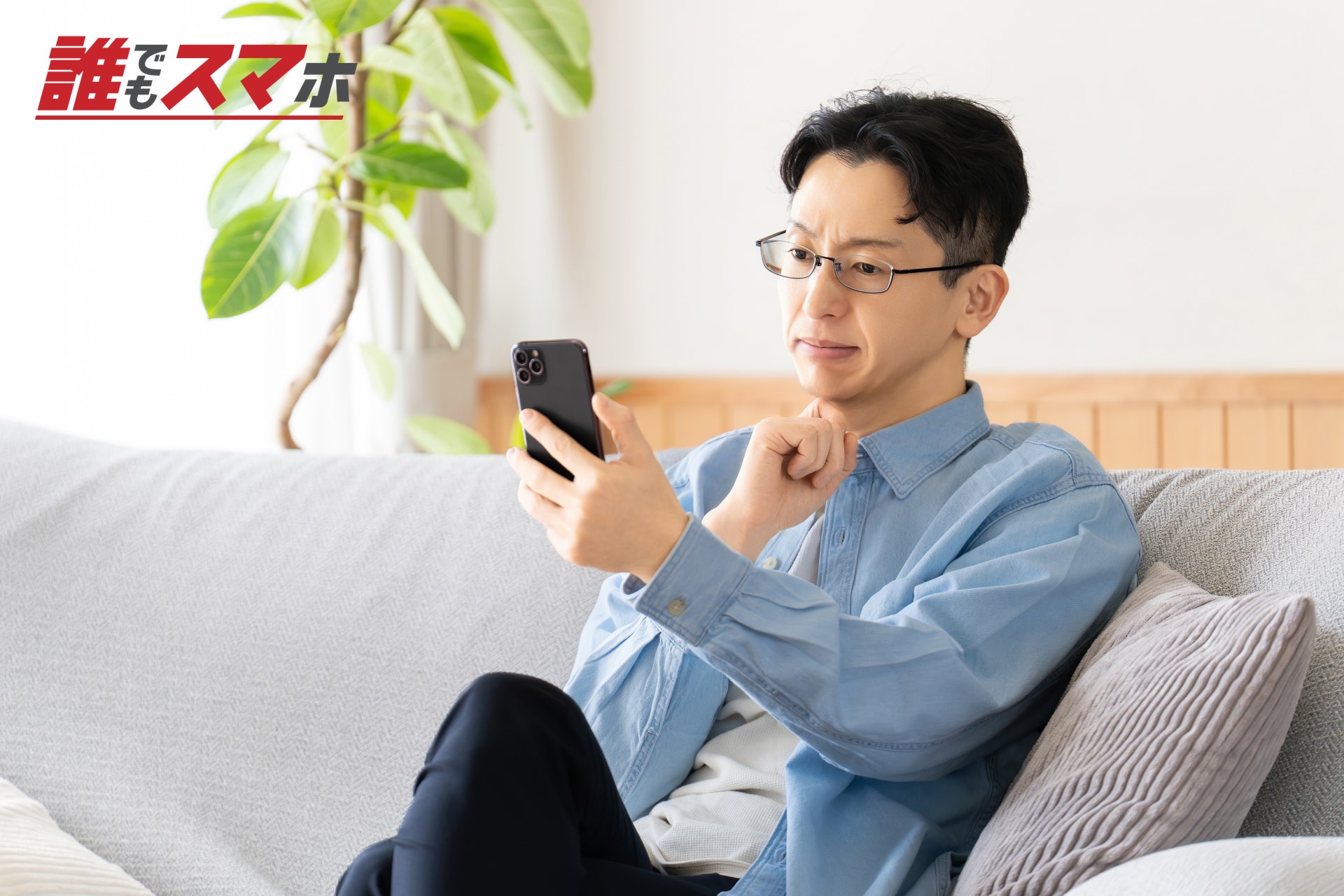ソファでスマートフォンを見て考える男性